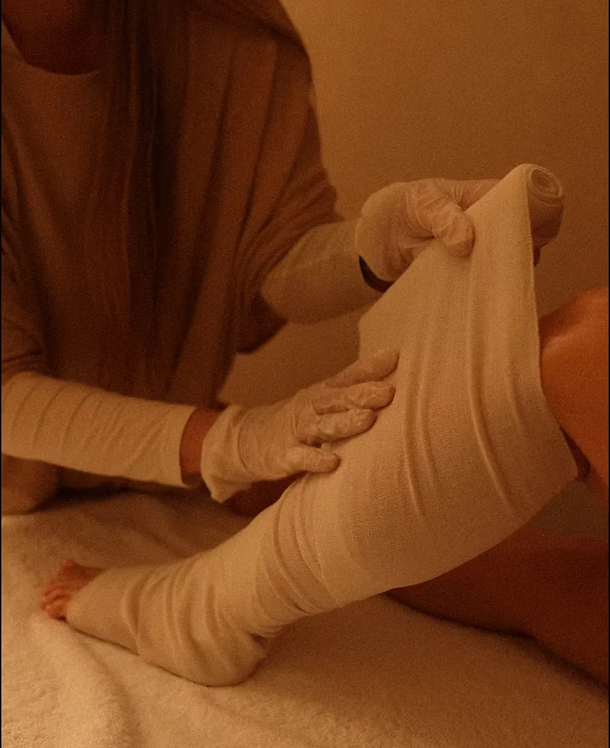 Therapist wrapping the leg in a warm herbal bandage during a hot anti-cellulite STYX wrap